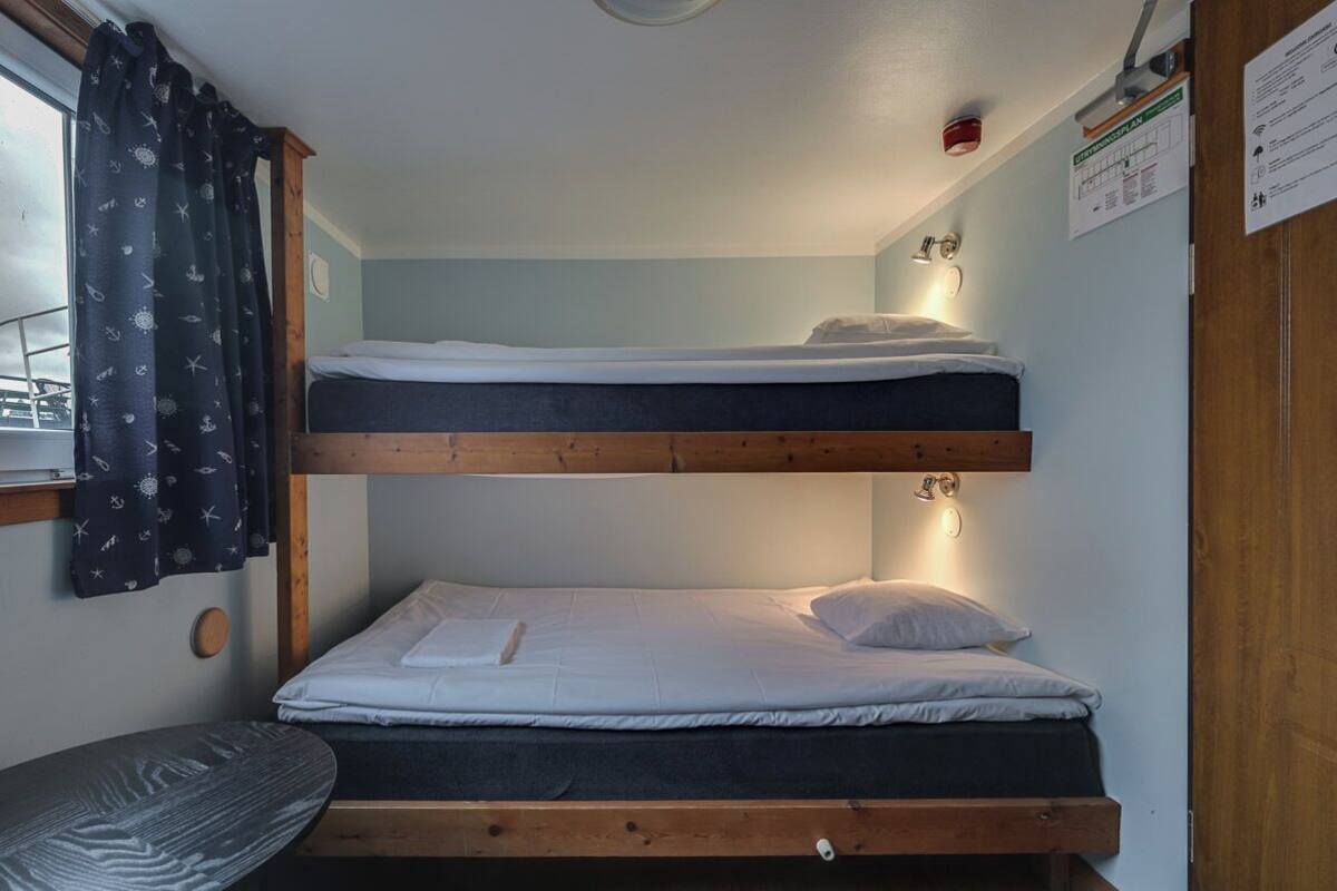 A bunk bed room with a window, a small table, and a wall-mounted light.