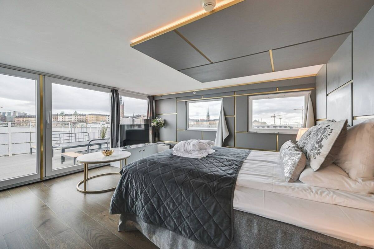 A modern hotel room with a large bed, a round table, and a city view through floor-to-ceiling windows.