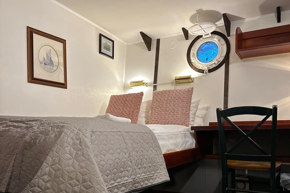 A bedroom with a bed, a desk, and a chair. There are wall-mounted lamps and a framed picture on the wall.