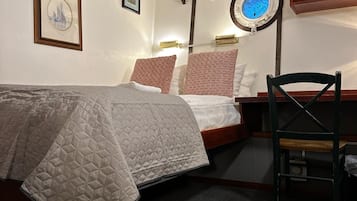 Une chambre à coucher avec un lit, un bureau et une chaise. On y trouve des lampes fixées au mur et un tableau encadré accroché au mur.