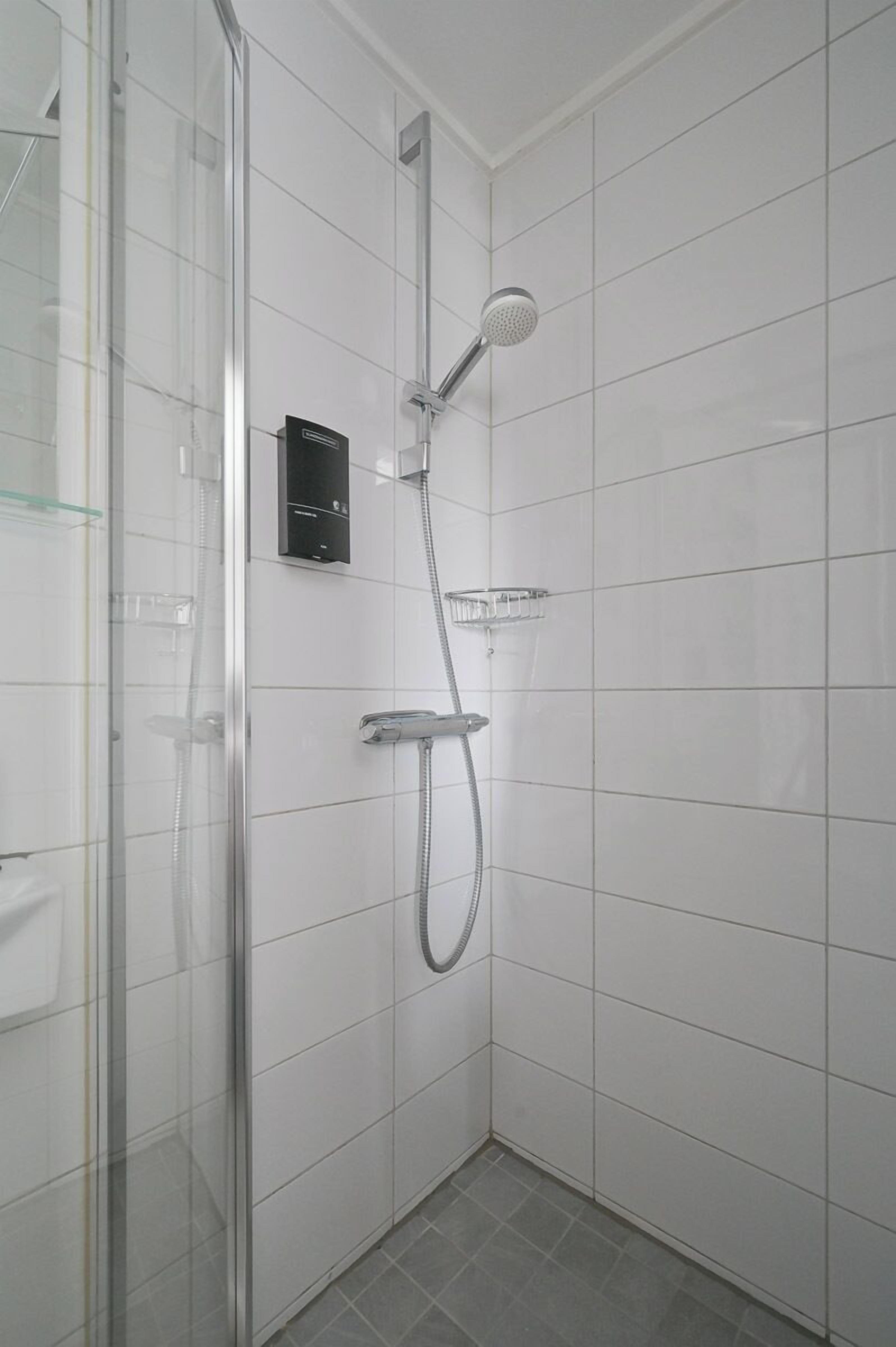 Una ducha moderna con cabina de vidrio, cabezal de ducha de mano y panel de control empotrado.