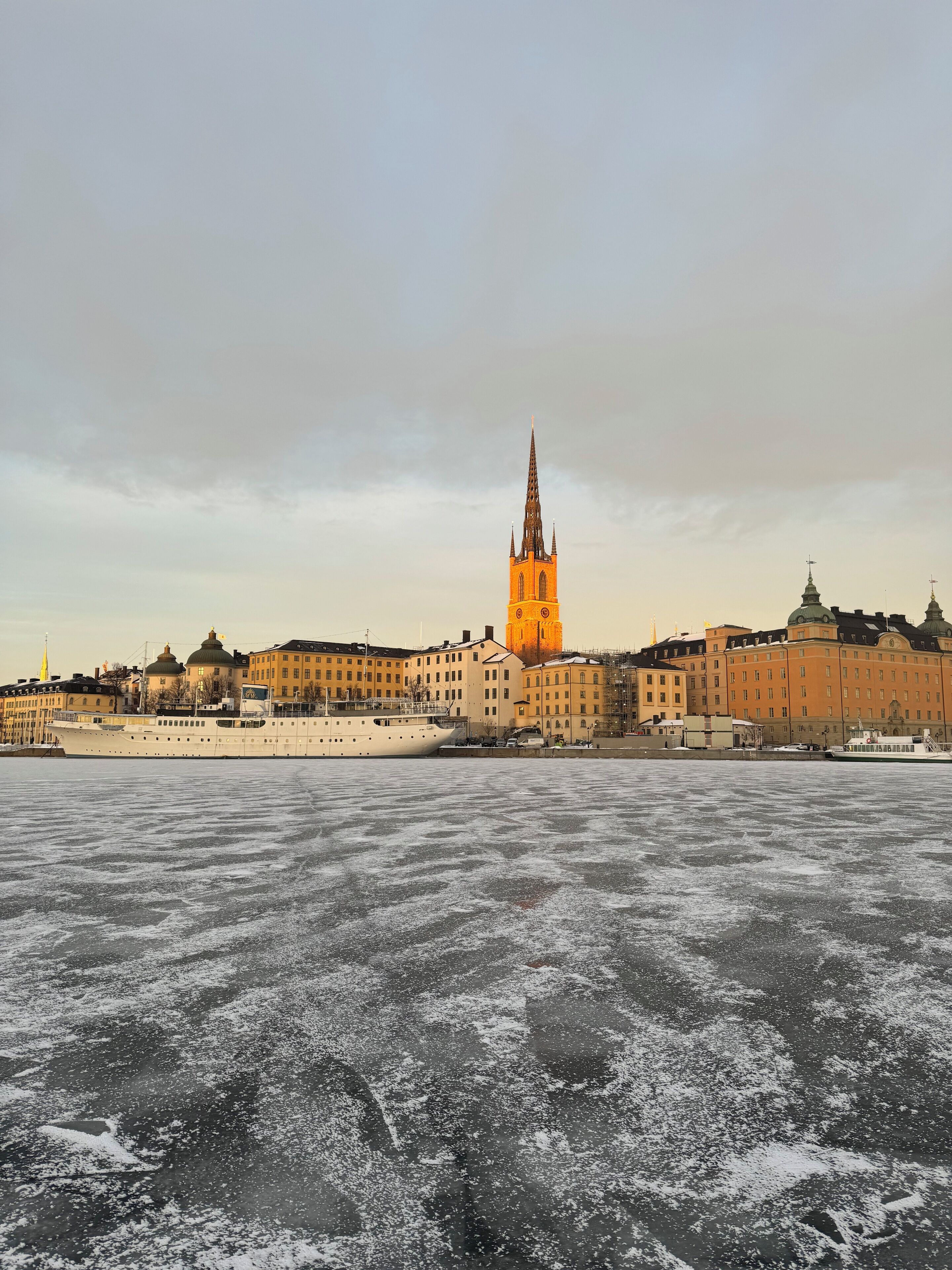 A waterfront cityscape with a prominent church spire, buildings along the riverbank, and a frozen river.