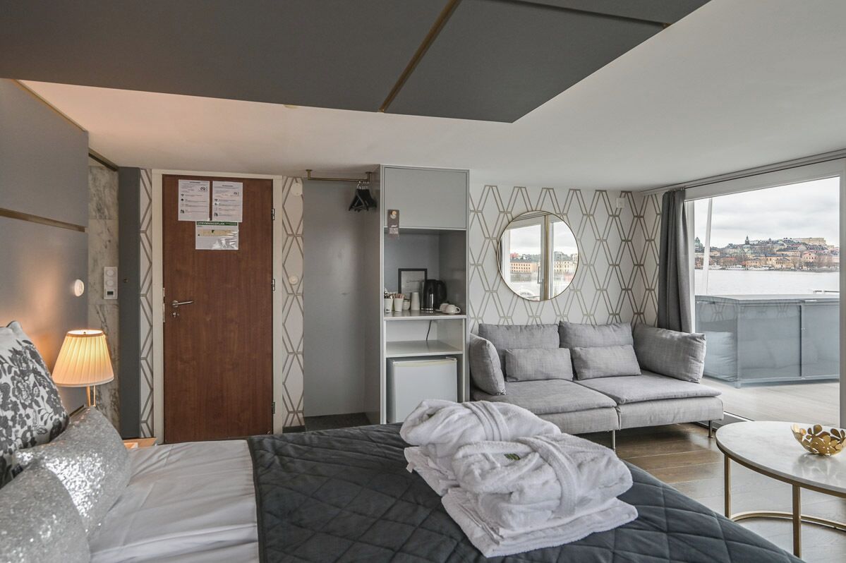 Ett modernt hotellrum med en säng, en soffa, ett litet bord och utsikt över stadsbilden.