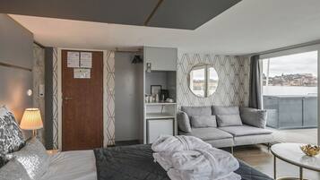 Ett modernt hotellrum med en säng, en soffa, ett litet bord och utsikt över stadsbilden.