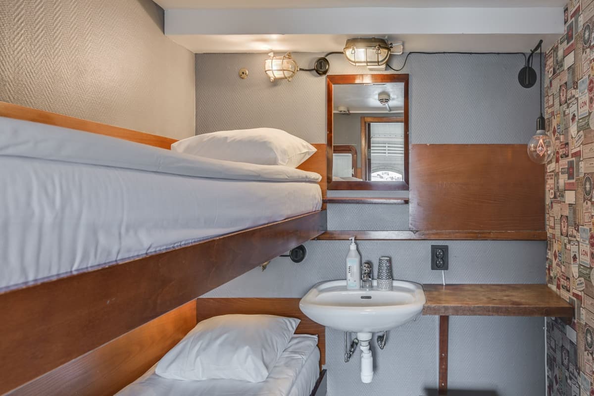 A compact hotel room with a bunk bed, a small sink, and a mirror.