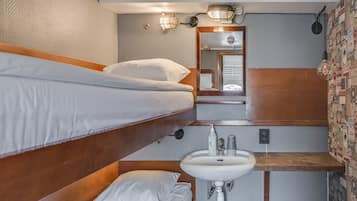 A compact hotel room with a bunk bed, a small sink, and a mirror.