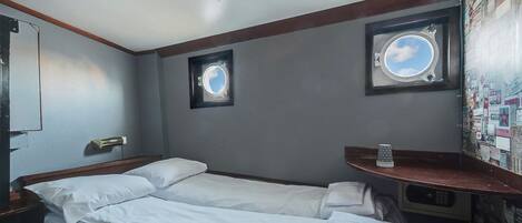 A room with two single beds, a small window, a mirror, and a wall with a bulletin board.