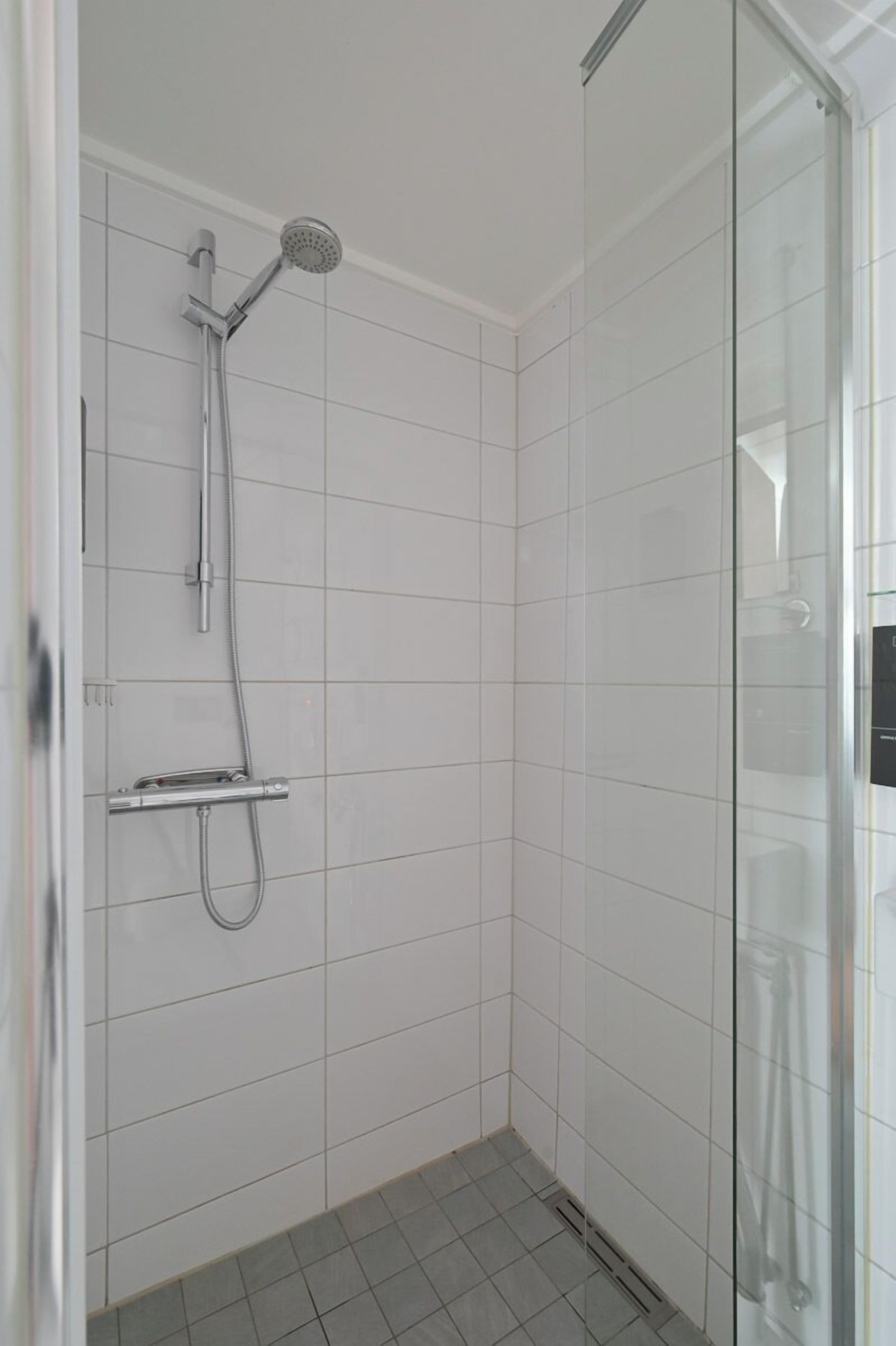 Un baño pequeño con azulejos, puerta de vidrio y ducha de mano.