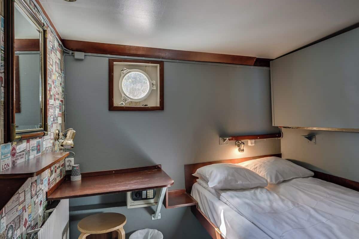 A compact hotel room with a small desk, a bed, a window with a view, and a mirror.