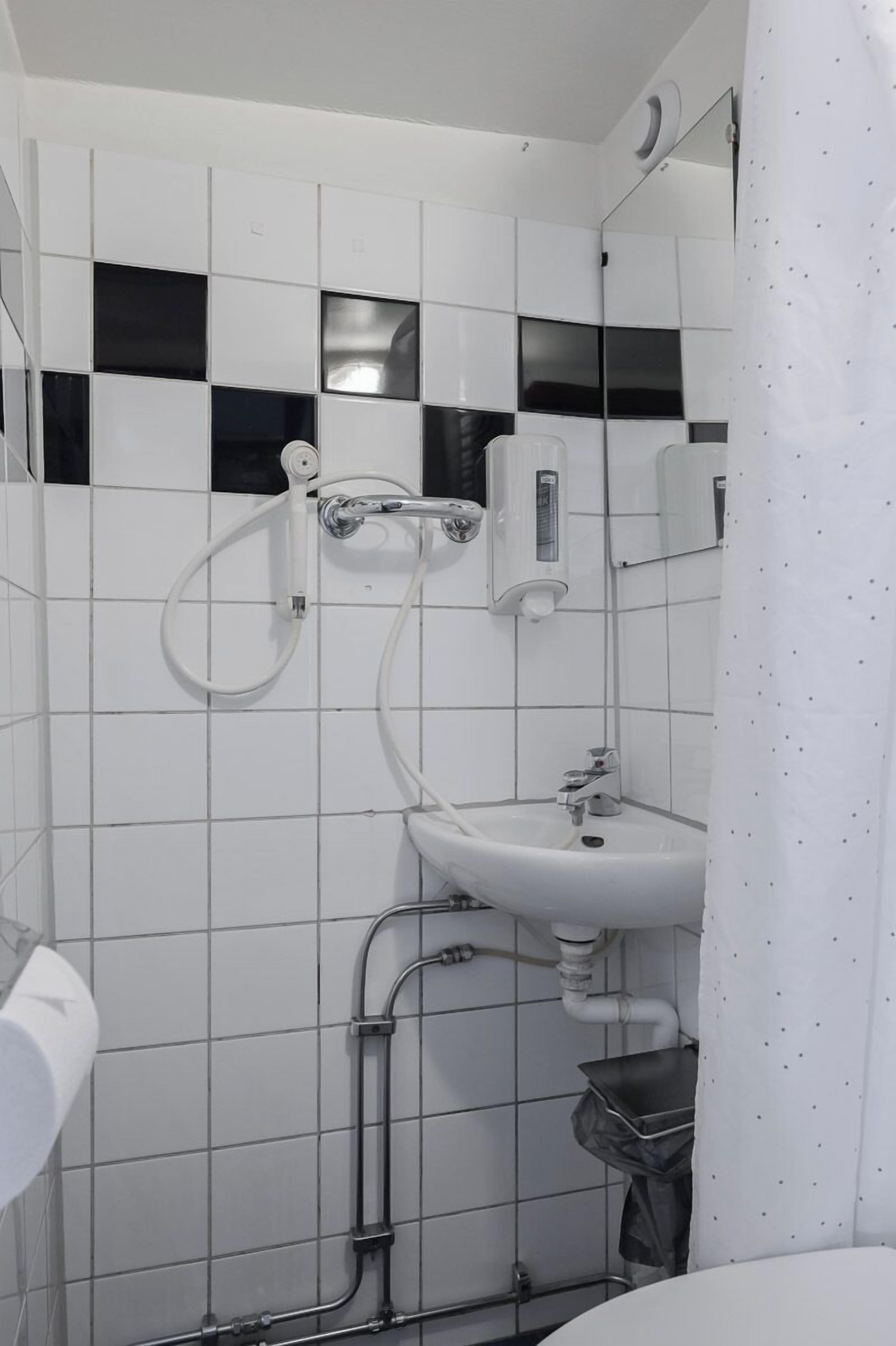 Un baño con paredes de azulejos blancos, un lavabo, un espejo y una ducha.