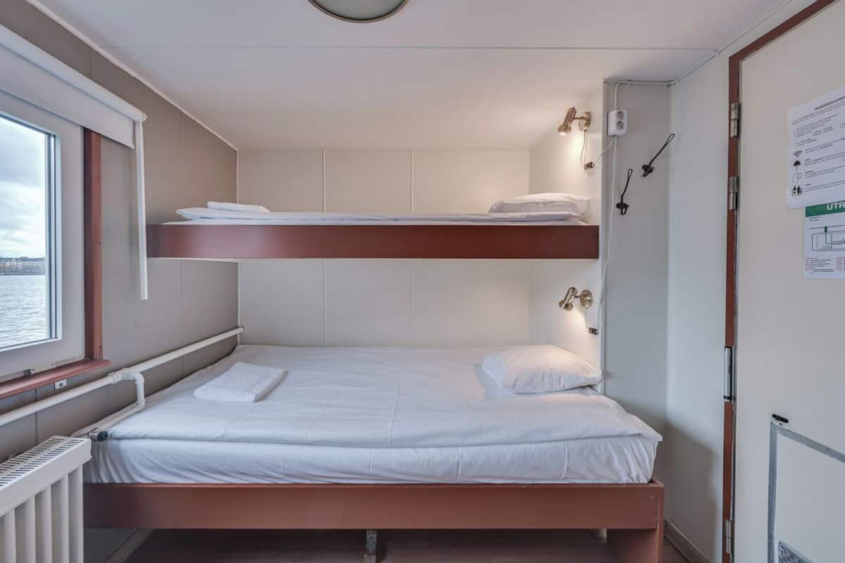 A compact cabin with a bunk bed, a window with a view of the water, and a small bathroom with a mirror and towel rack.