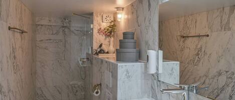 A modern bathroom with a glass-enclosed shower, marble walls, and a gold sink.