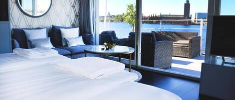 Una habitación de hotel moderna con una cama grande, un espejo redondo, un sofá y un balcón con vista a un cuerpo de agua y un faro.