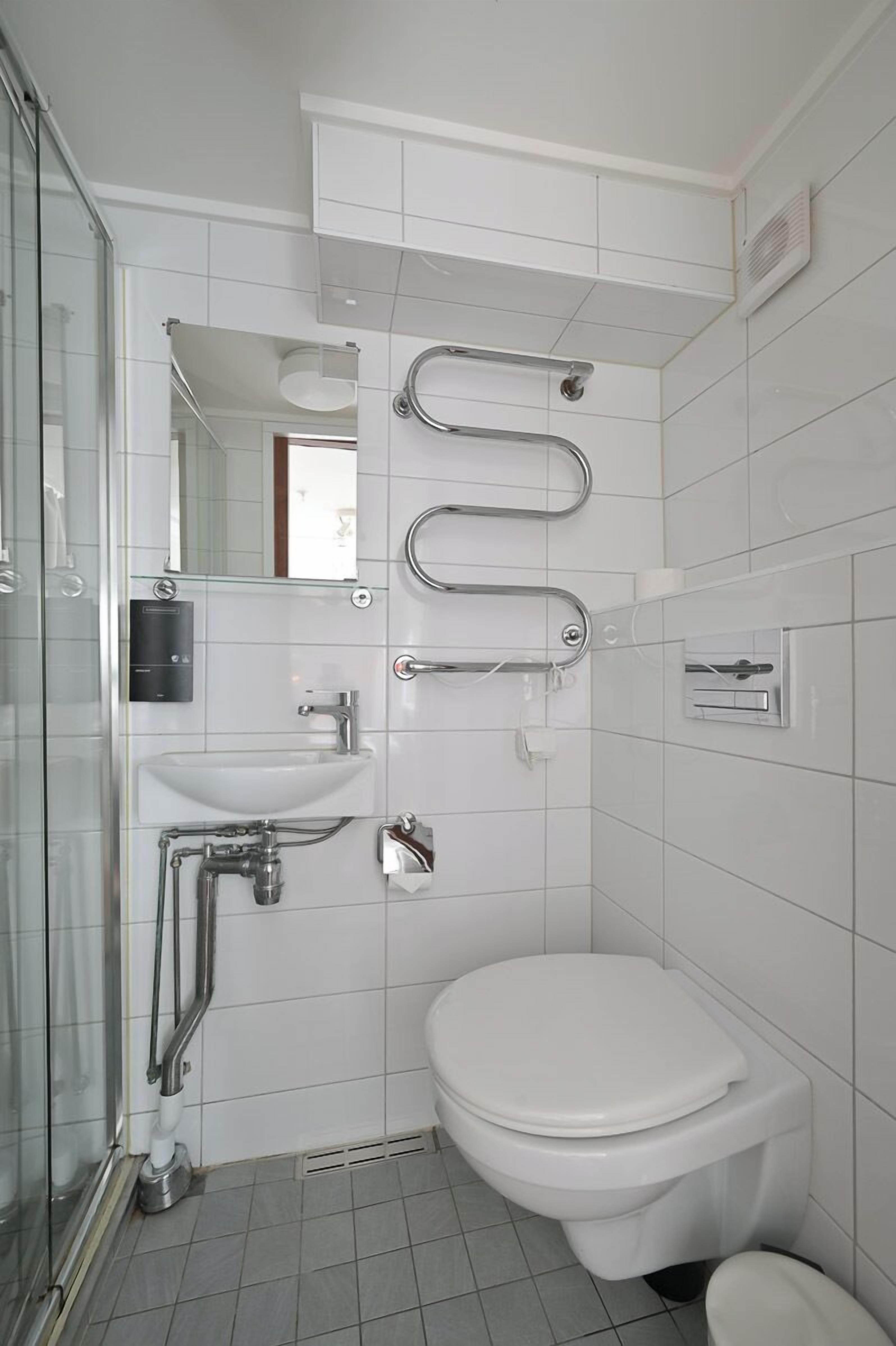 Un baño moderno con cabina de ducha de vidrio, un lavabo blanco, un inodoro y un pasamanos.