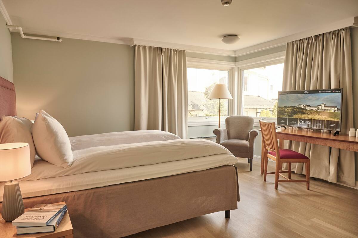 A hotel room with a bed, a desk, a chair, a TV, and a lamp.
