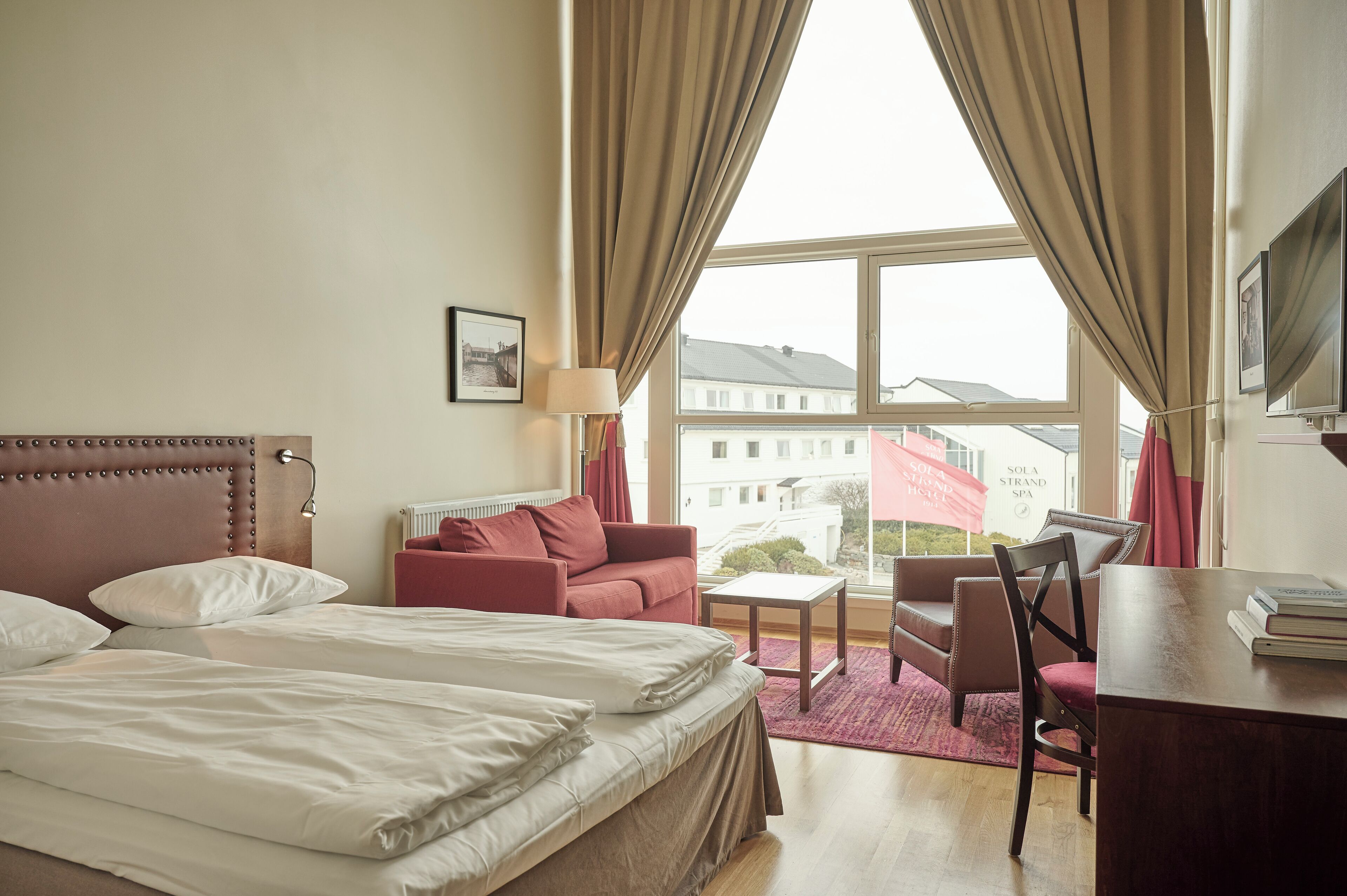 A hotel room with a bed, a red sofa, a small table, a chair, and a desk.