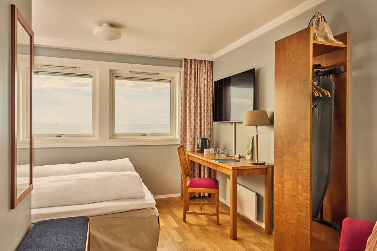 A hotel room with a bed, desk, chair, and a television.