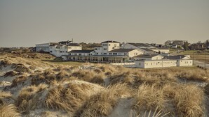 A large, modern building with multiple sections, surrounded by sand dunes and sparse vegetation. - Sola Strand Hotel (Sola)