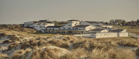 A large, modern building with multiple sections, surrounded by sand dunes and sparse vegetation.