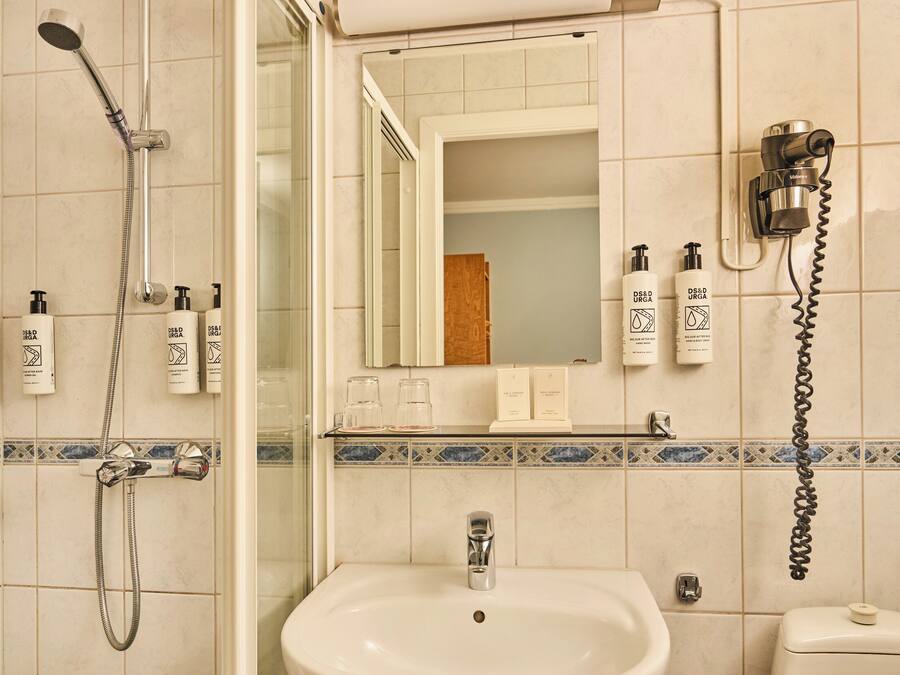 Une salle de bain avec une douche, un lavabo et des toilettes. On y trouve des articles de toilette accrochés au mur et un miroir au-dessus du lavabo.