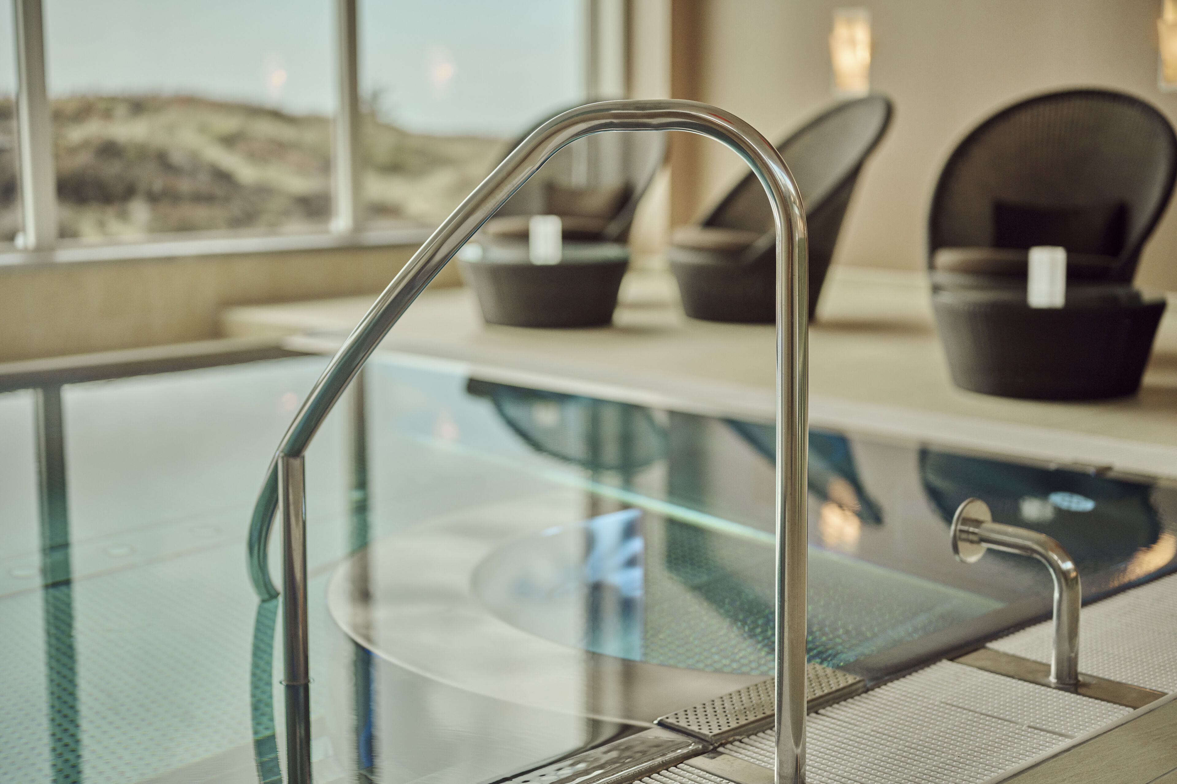 Ein moderner Poolbereich im Innenbereich mit Glasbarriere und Metallgeländern.
