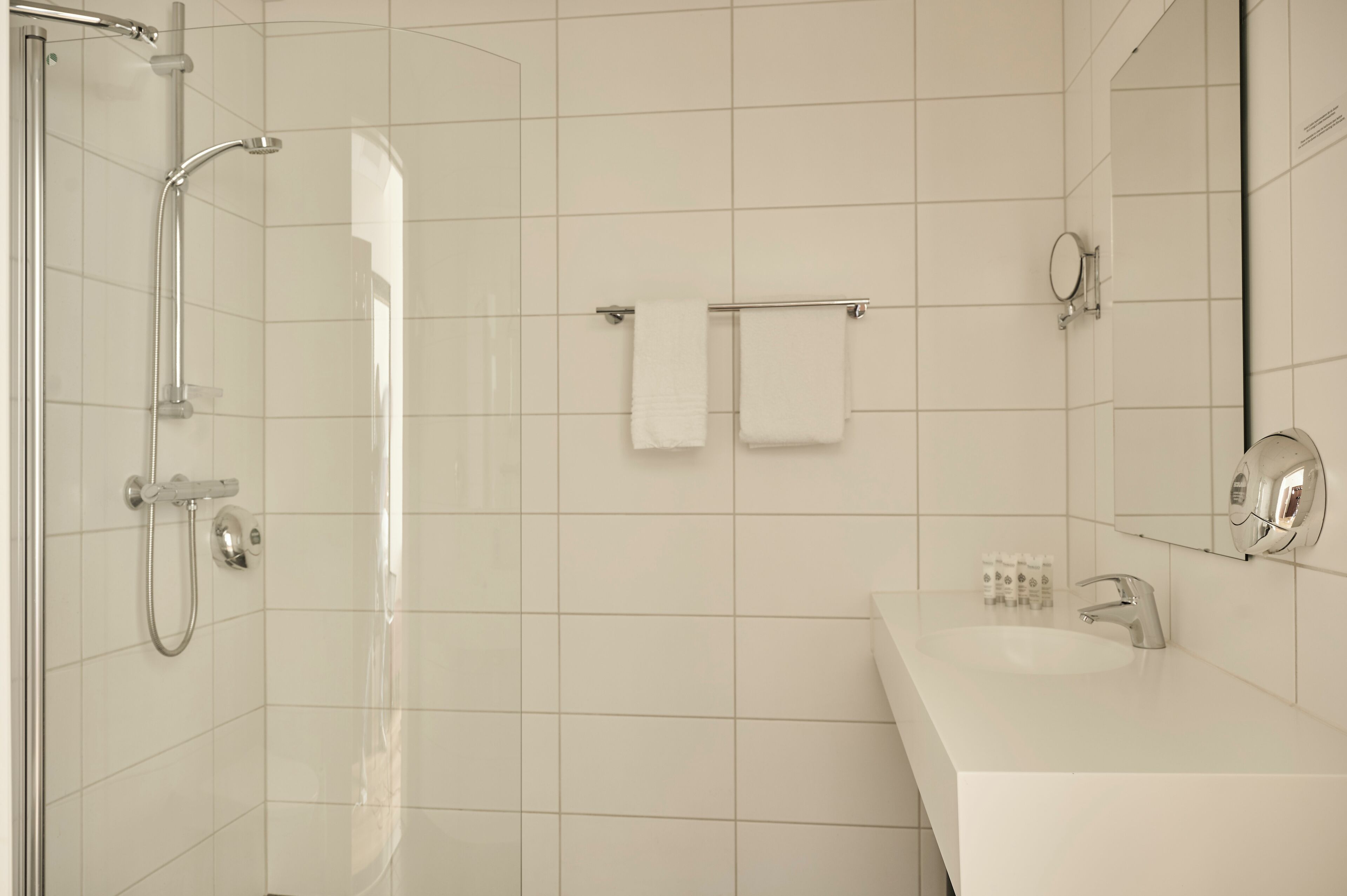 Uma casa de banho moderna com cabine de duche em vidro, uma sanita branca e um espelho.