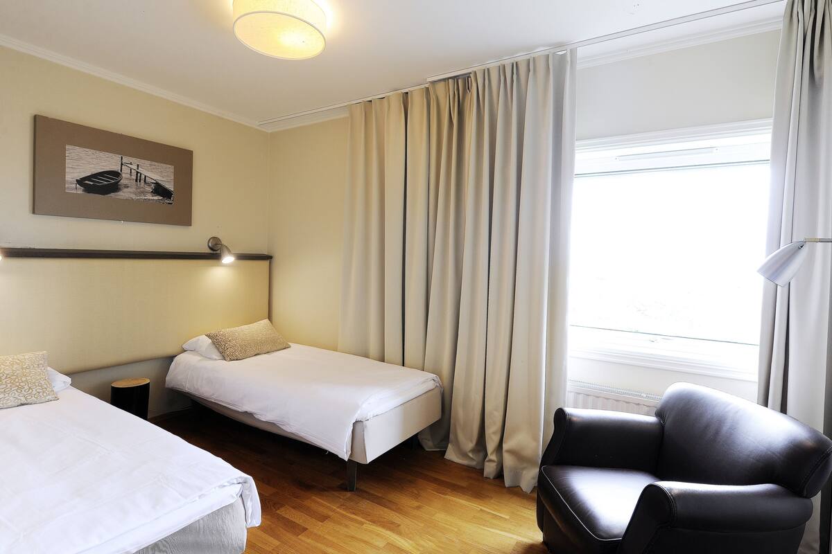 A hotel room with two beds, a chair, a lamp, and a painting on the wall.
