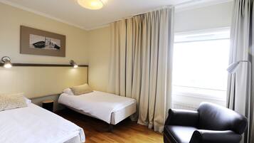 A hotel room with two beds, a chair, a lamp, and a painting on the wall.