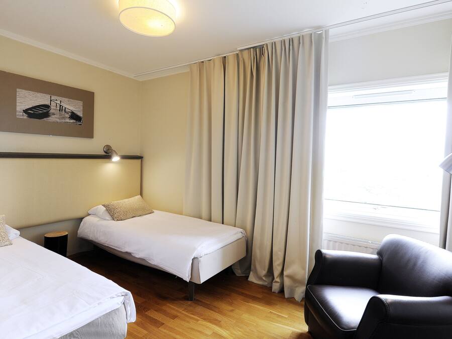 A hotel room with two beds, a chair, a lamp, and a painting on the wall.
