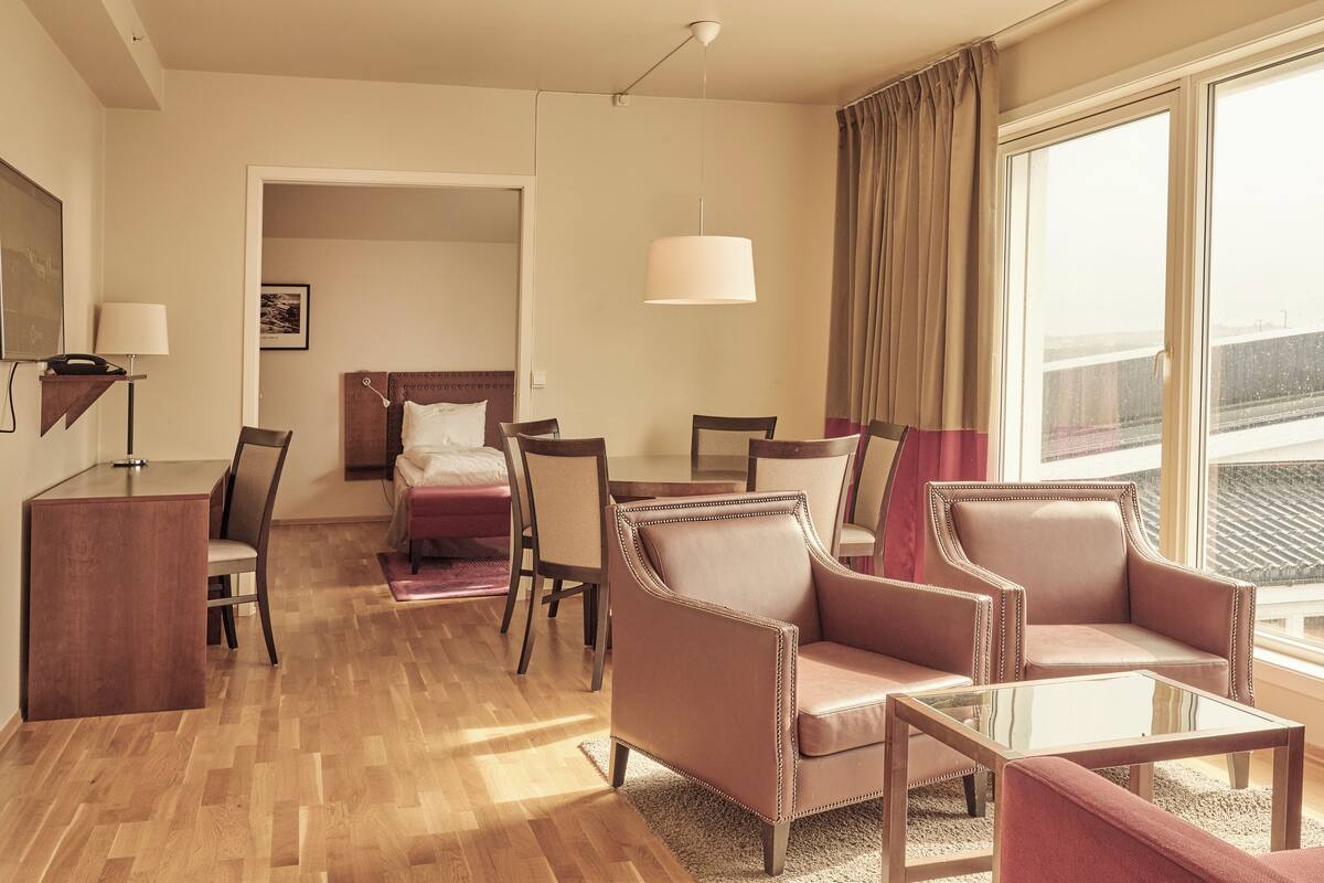 A hotel room with a bed, two armchairs, a coffee table, a desk, and a lamp.