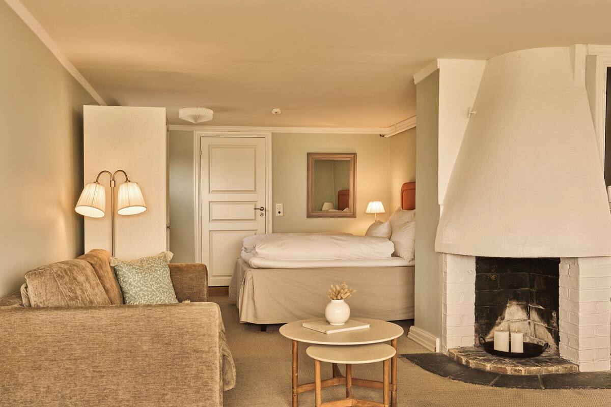 A cozy room with a bed, a sofa, a small table with a vase, and a fireplace.