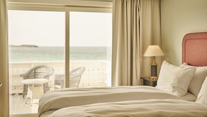 A hotel room with a bed, a nightstand with a lamp, a chair, and a view of the sea through a large window. - Sola Strand Hotel (Sola)