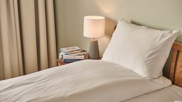 A neatly made bed with white linens, a bedside lamp, and a stack of books on a nightstand.