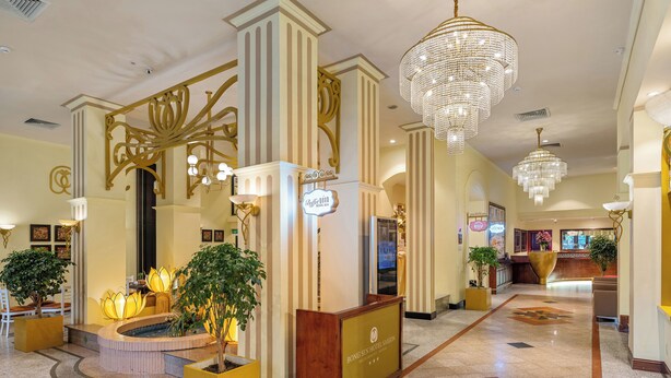 A hotel lobby with a reception desk, a large chandelier, and a decorative floor pattern.