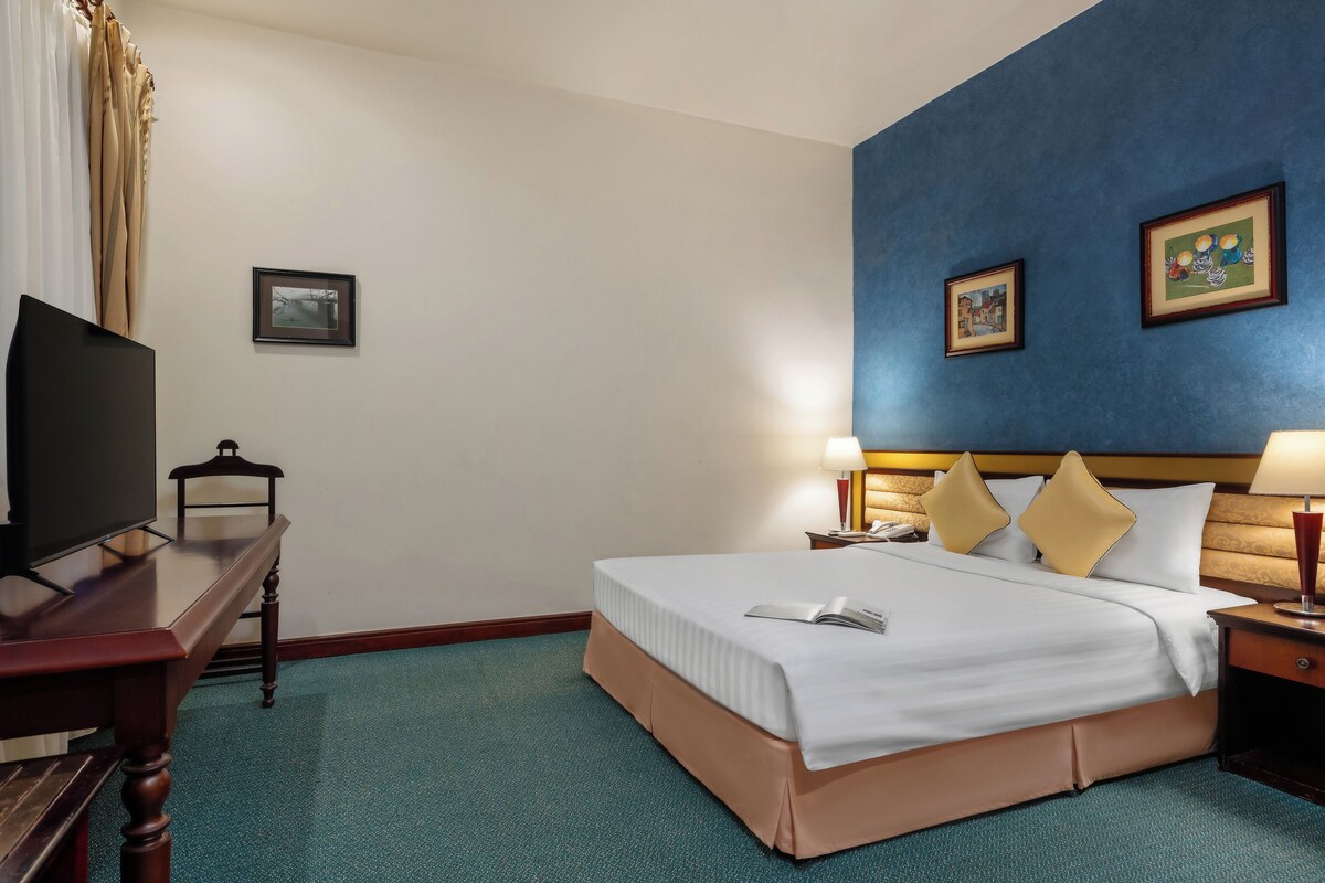 A hotel room with a bed, a desk, a television, and two paintings on the wall.