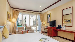 A hotel room with a large bed, a desk, a TV, and a view of the city.