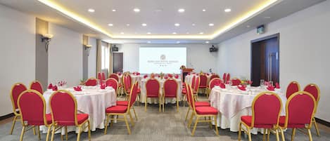 A conference room with round tables, red chairs, and a presentation screen.