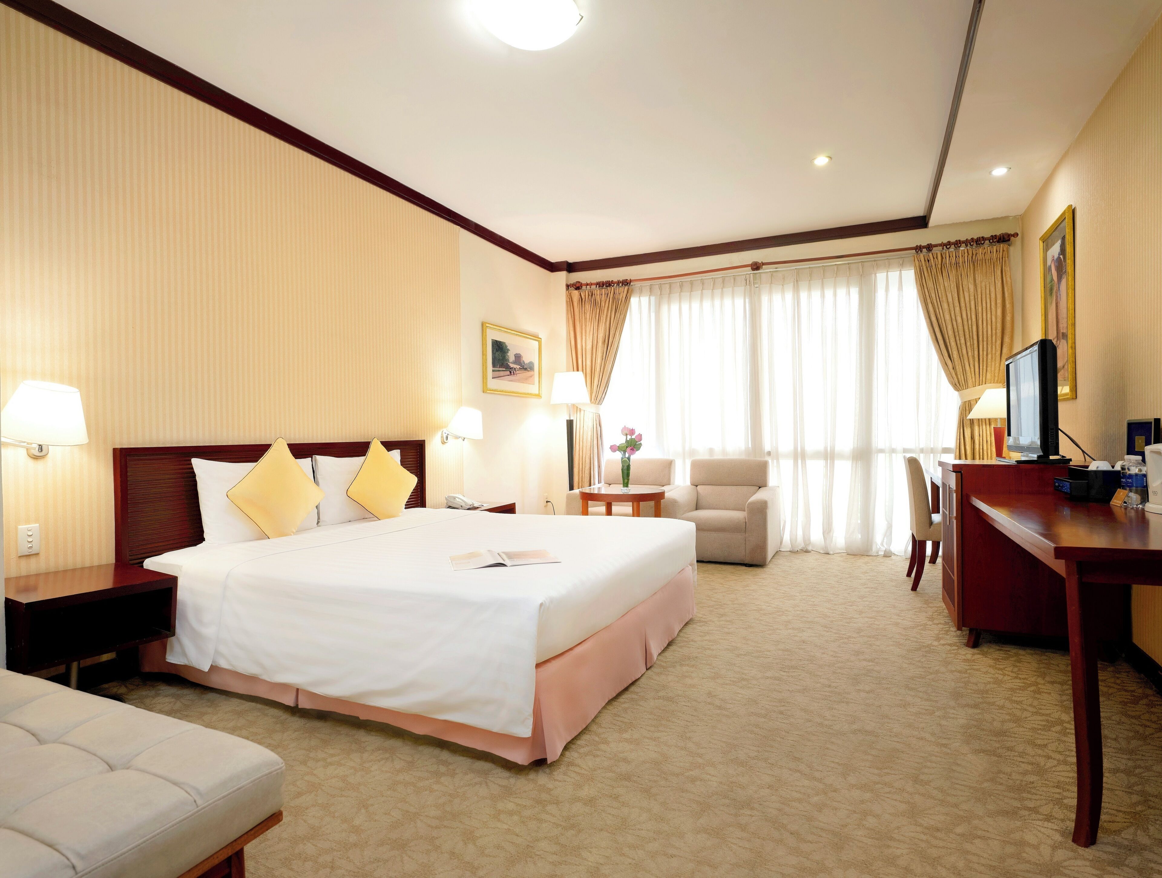 Quarto de hotel com uma cama grande, uma escrivaninha com computador, uma cadeira e um sofá.