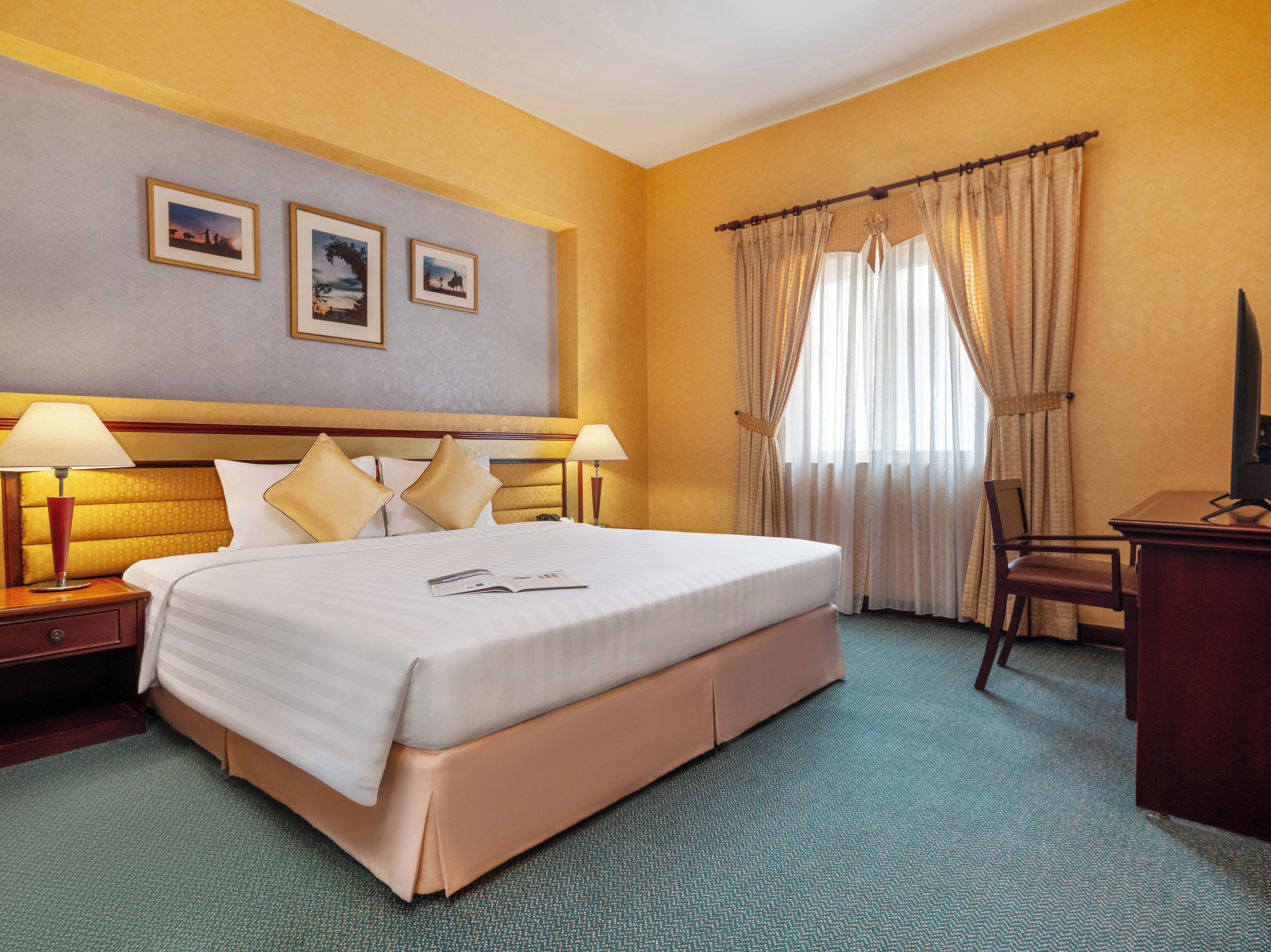 A hotel room with a large bed, two bedside lamps, a desk with a chair, and a window with curtains.