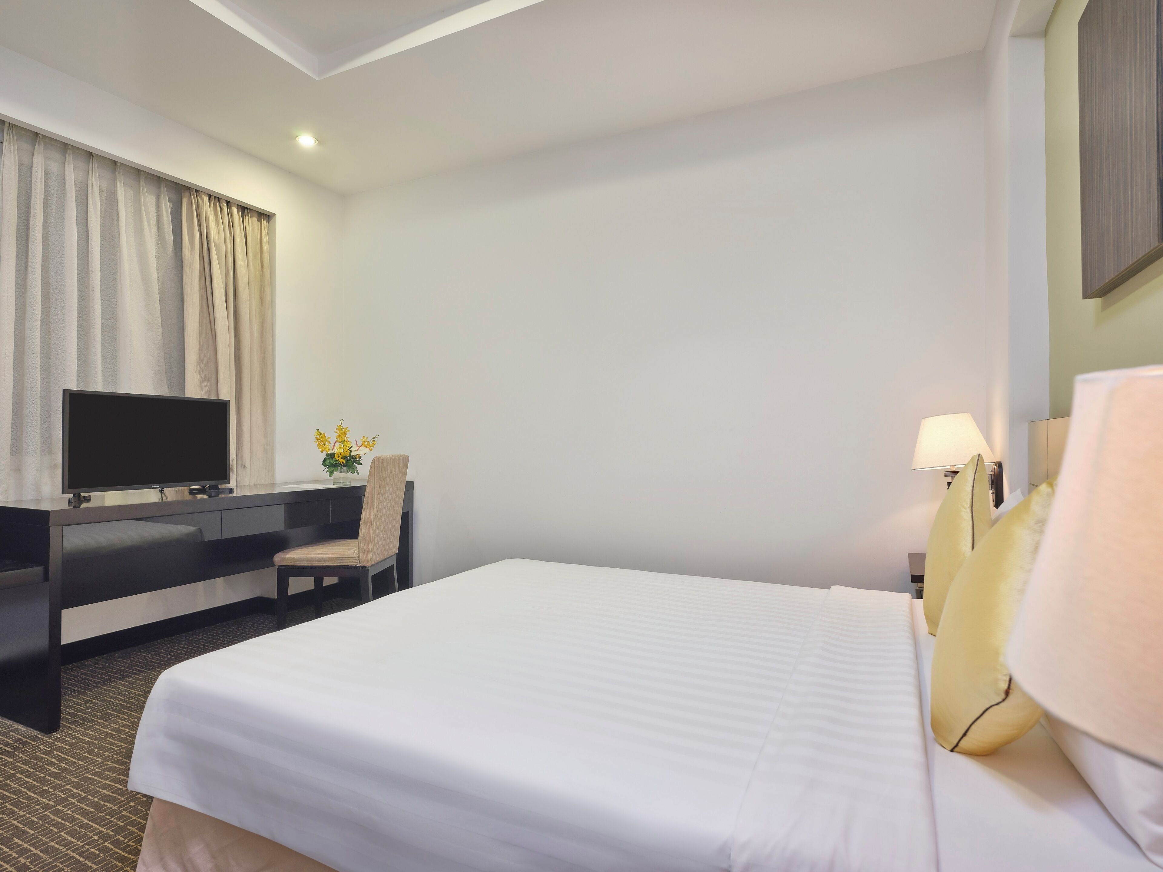 A hotel room with a bed, a desk with a chair, a television, and a lamp.