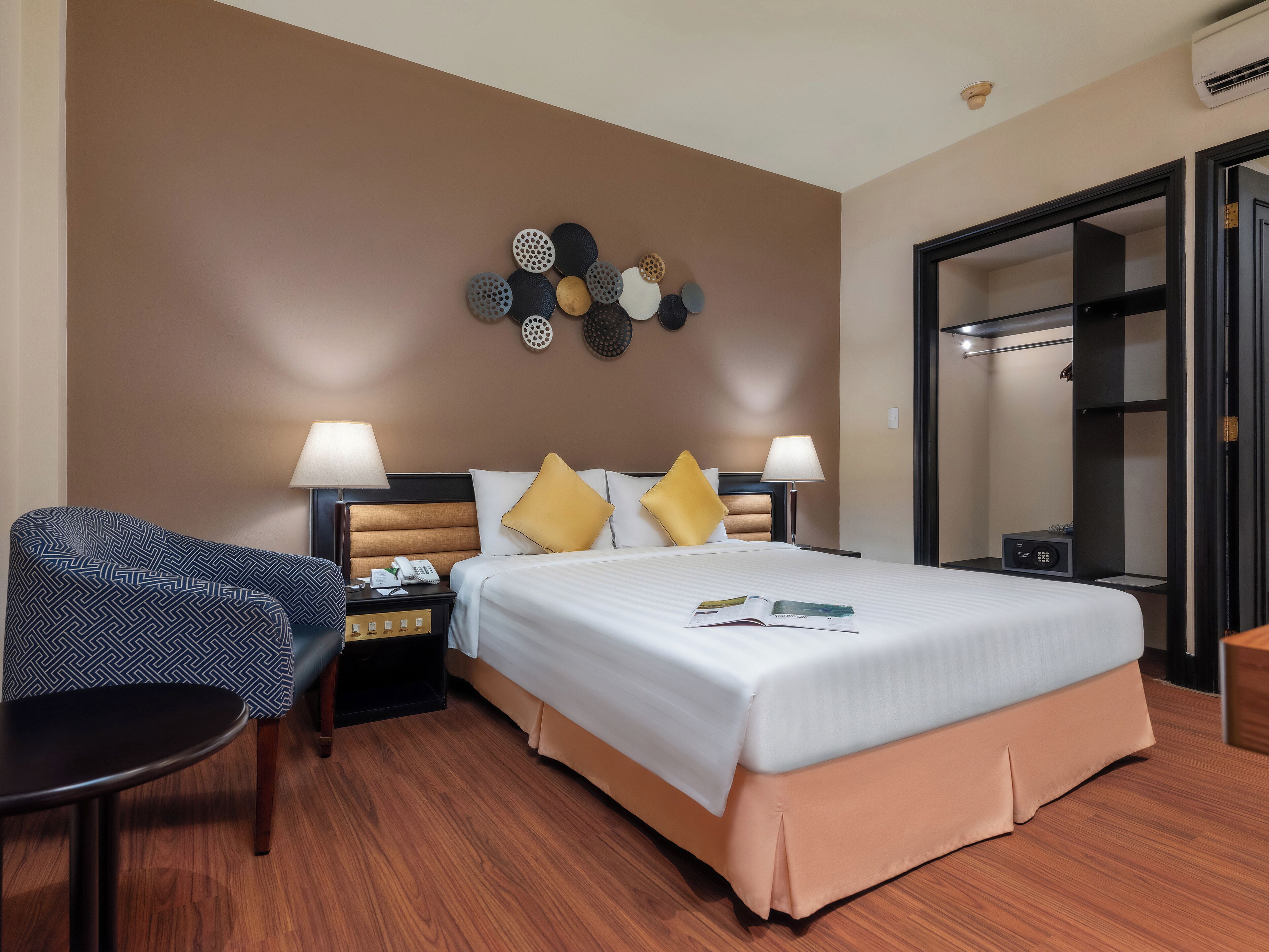 Una habitación de hotel con una cama, dos mesitas de noche, una silla, una obra de arte en la pared y una puerta.