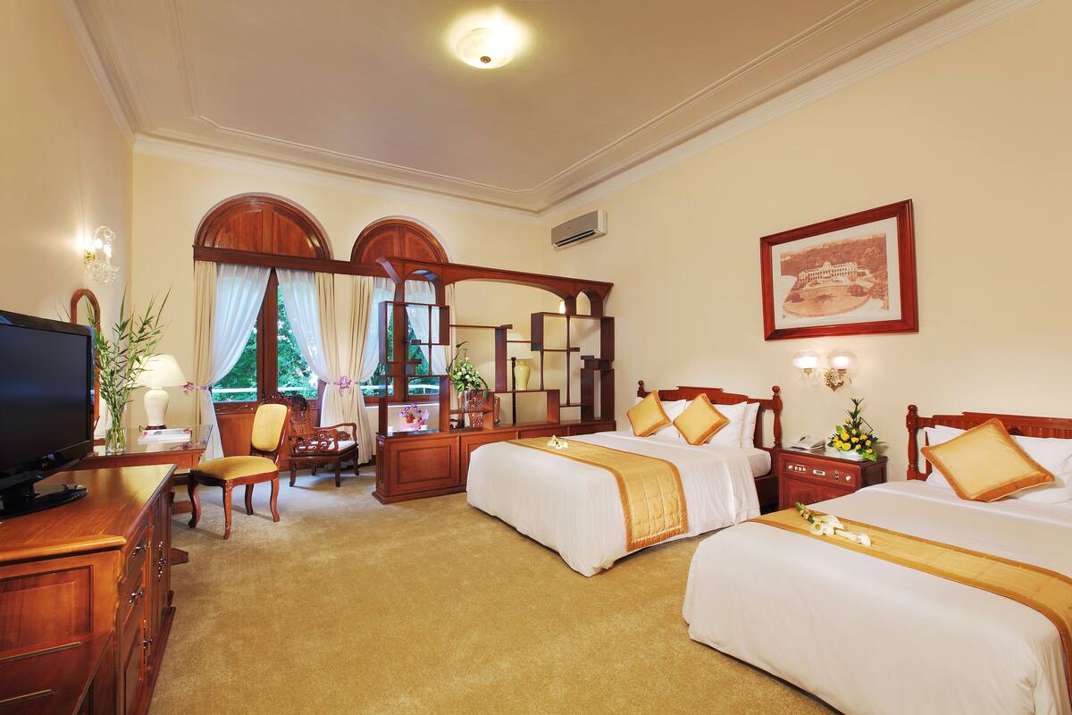 Une chambre d’hôtel avec deux lits, un bureau avec une télévision, une chaise et une grande fenêtre avec des rideaux.