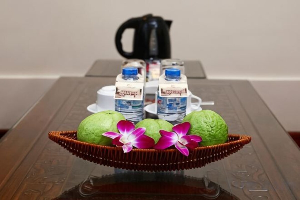 A table with a basket containing green fruits and two bottles of water, a coffee pot, and a cup in the background.
