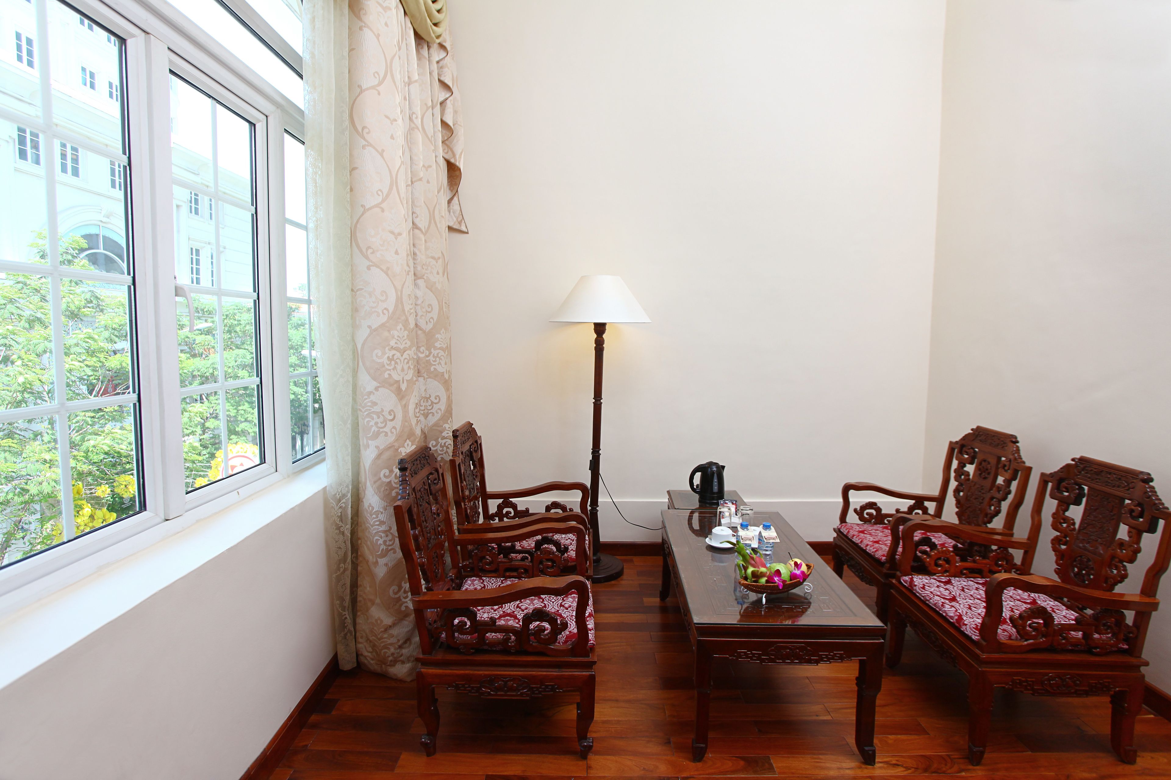 A room with two wooden chairs, a table with a lamp, and a view of greenery outside a window.