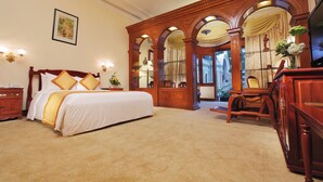 A spacious bedroom with a large bed, wooden furniture, and a view through an arched window.