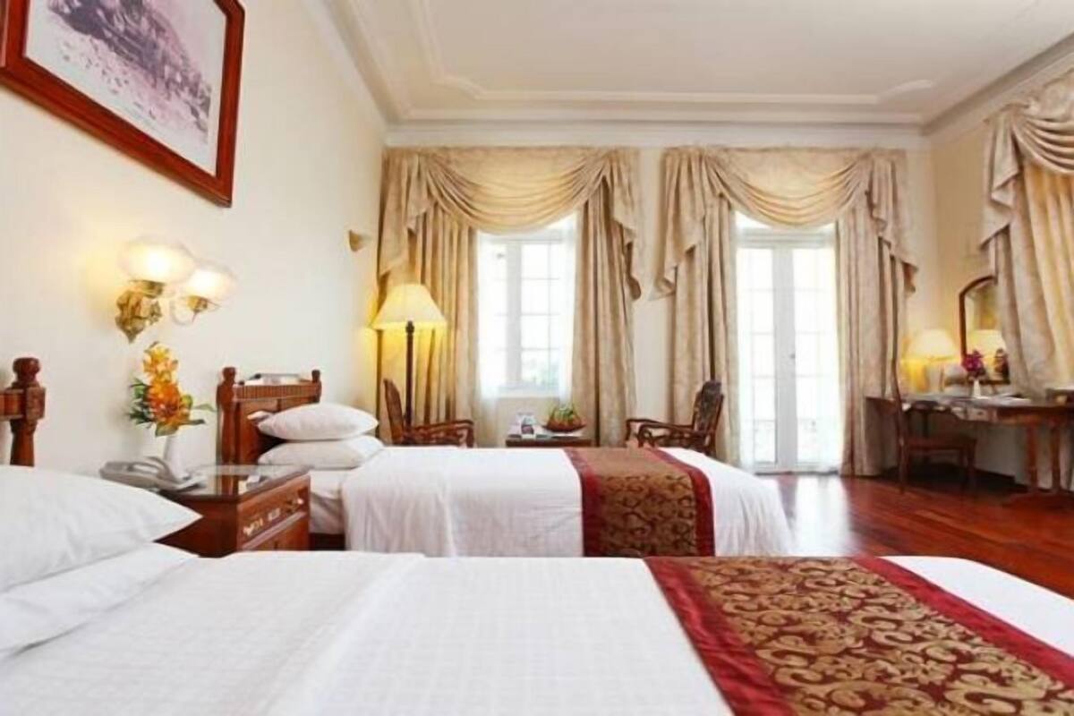 Une chambre d’hôtel avec deux lits, un bureau, une chaise et une grande fenêtre avec des rideaux.