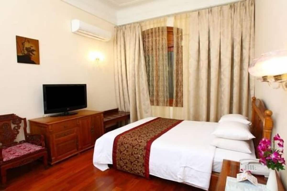 Une chambre d’hôtel comprenant un lit, une télévision, une commode en bois, un bureau avec une lampe et une fenêtre avec des rideaux.