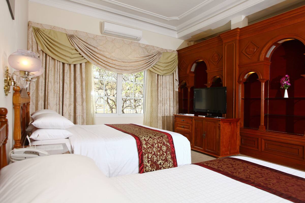 Une chambre d’hôtel avec deux lits, une télévision, une armoire en bois et une grande fenêtre avec des rideaux.