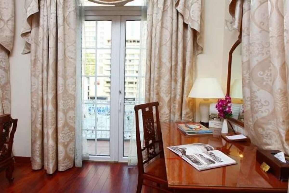A hotel room with a wooden desk, a chair, a lamp, a mirror, and a view through a glass door.