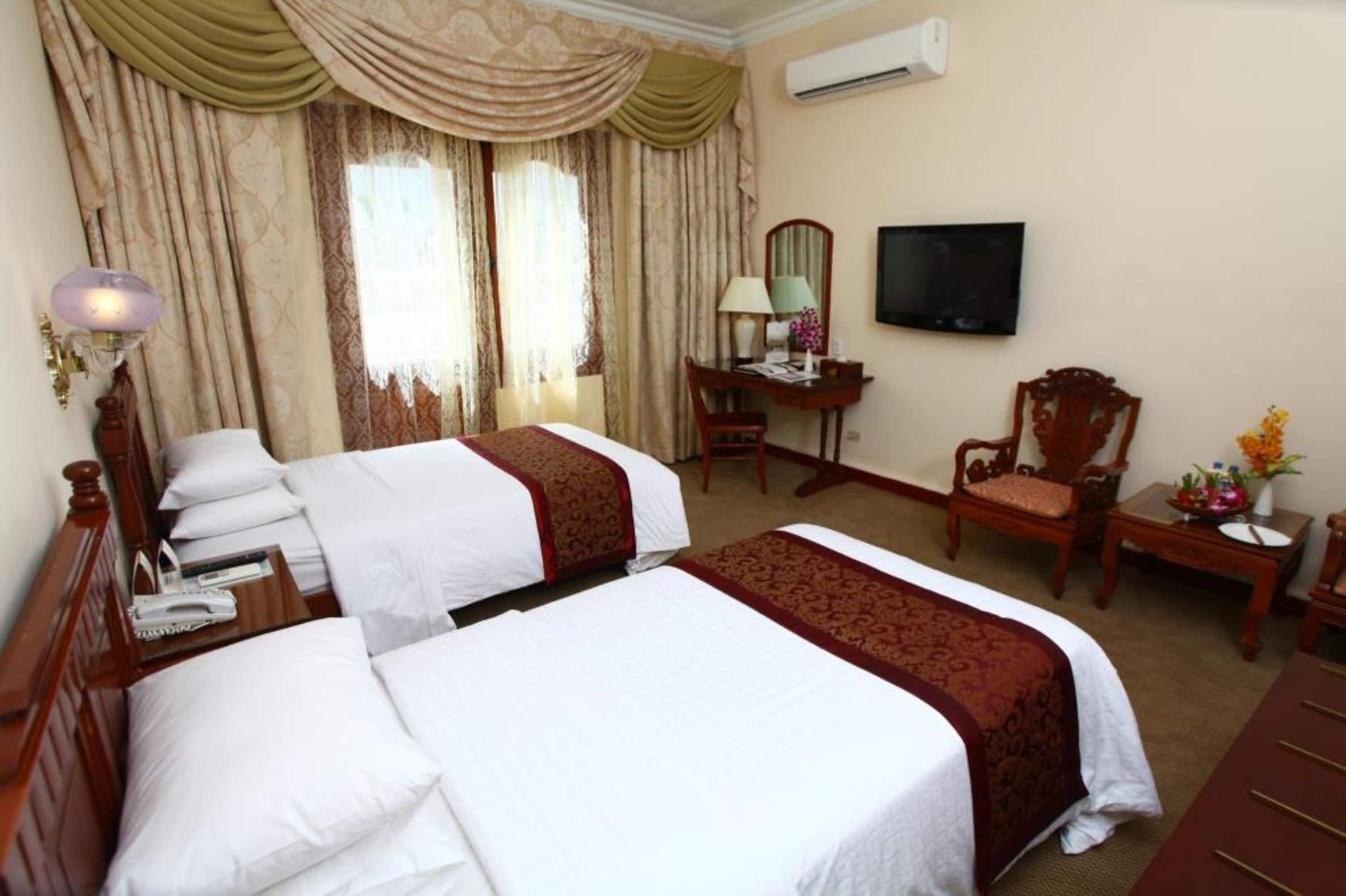 Une chambre d’hôtel avec deux lits, un bureau, une chaise, une télévision et une fenêtre avec des rideaux.